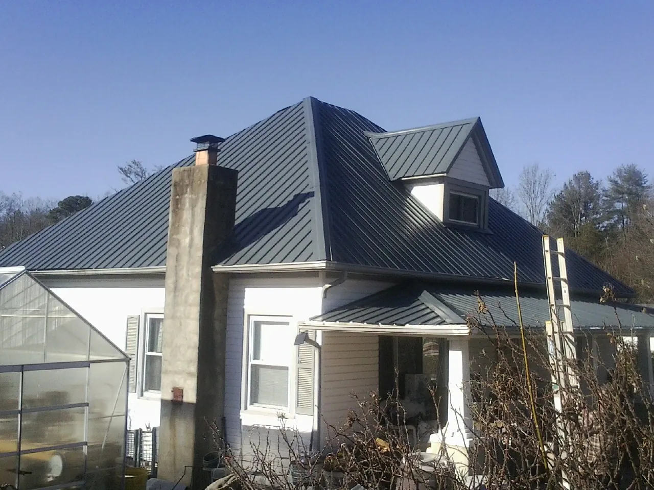 Dark blue standing seam metal roof on a white farmhouse with dormer — Slate & Tile Roof Repair by Roofing Brothers in Colona