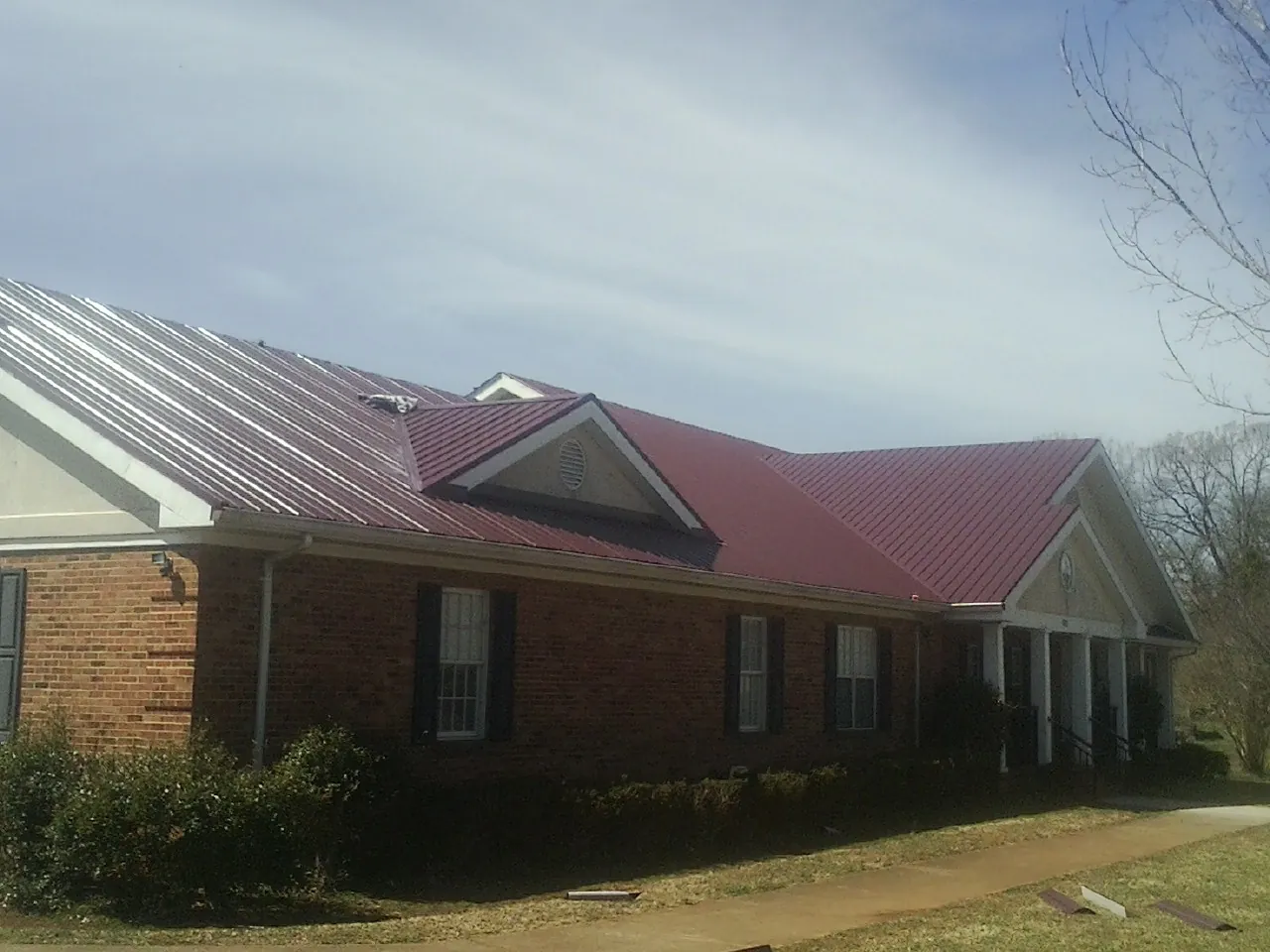 Red metal roof with gabled entries on a long brick building, from a Hail Damage Roof Repair job in Colona