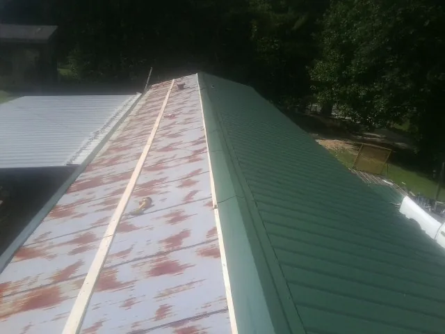 Old rusted panels beside newly installed green metal roofing — Wind Damage Roof Repair by Roofing Brothers in Colona