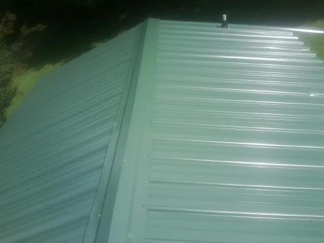New green metal panels meeting at the ridge of a roof — Flat Roof Repair work by our crew in Colona