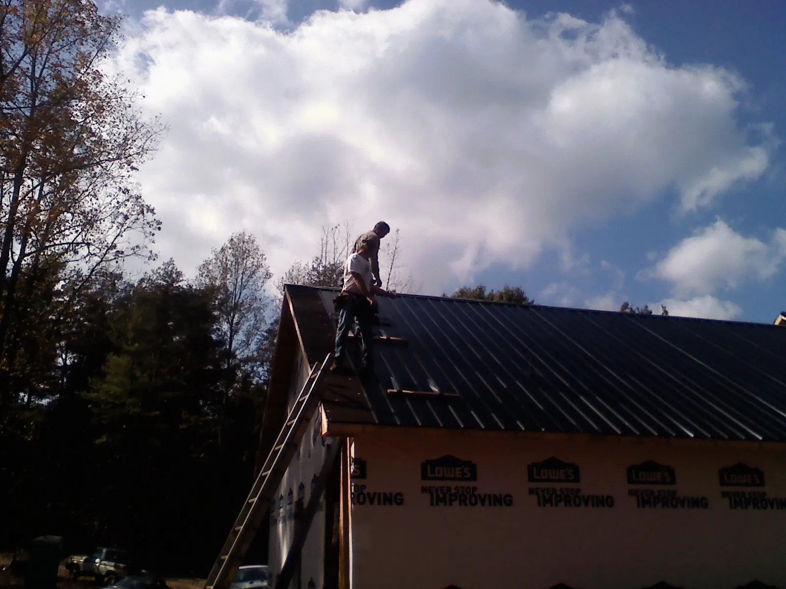 Roofer fastening dark metal panels high against a cloudy sky, from a Roof Inspection job in Colona