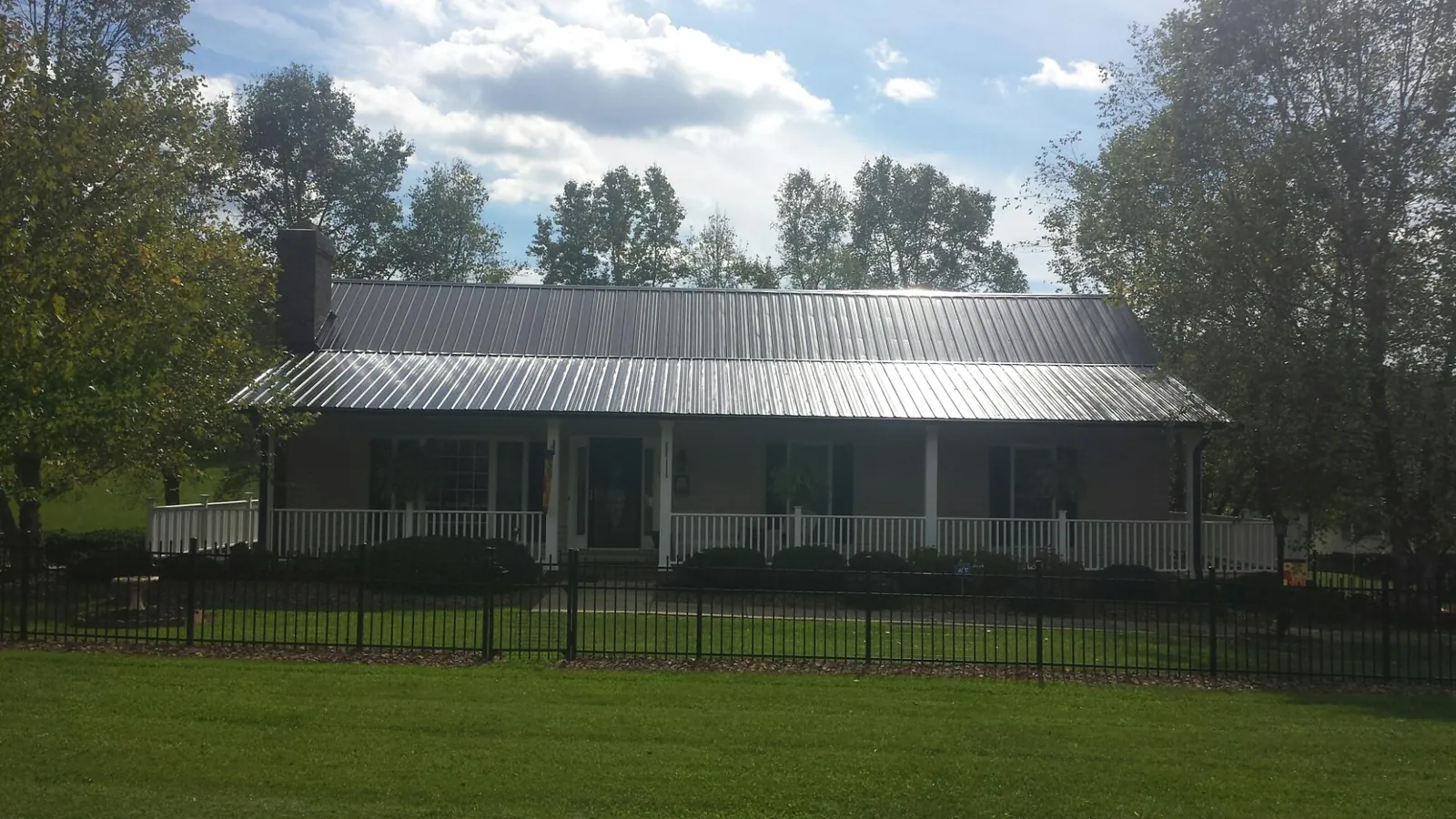 Gray metal roof on a brick ranch with a full width front porch — Gutter Guard Installation work by our crew in Colona