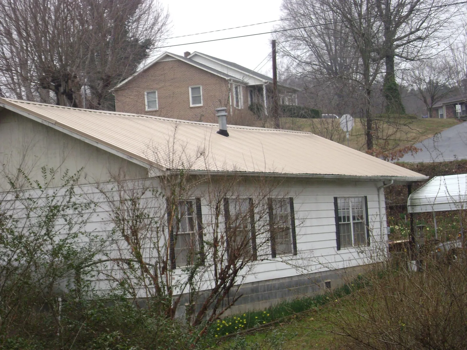 Tan metal roof on a white sided house set into a hillside — Commercial Roofing by Roofing Brothers in Colona
